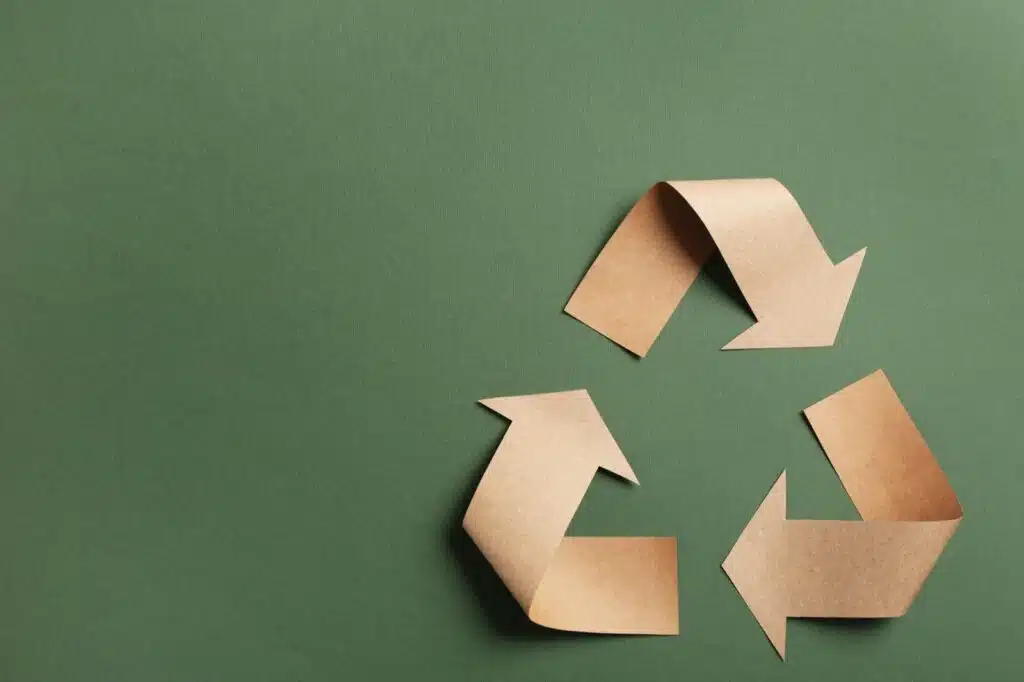 recycling symbol cut out of kraft paper on green background